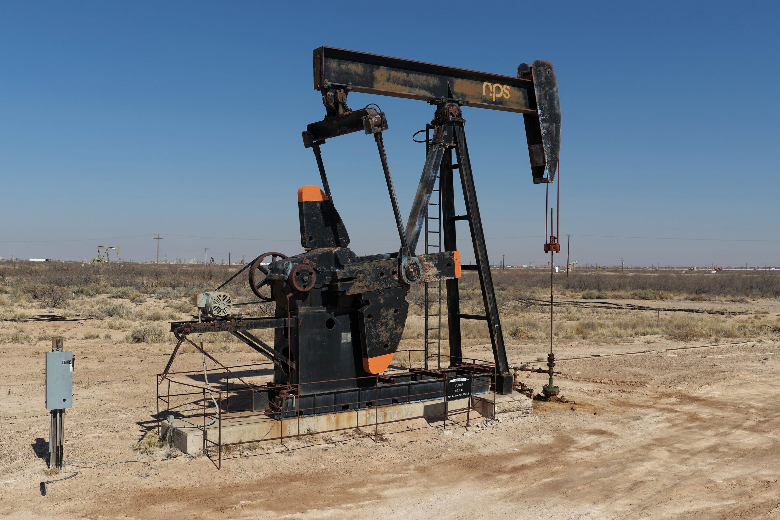 An oil pumpjack working in the Permian Basin under a clear blue sky