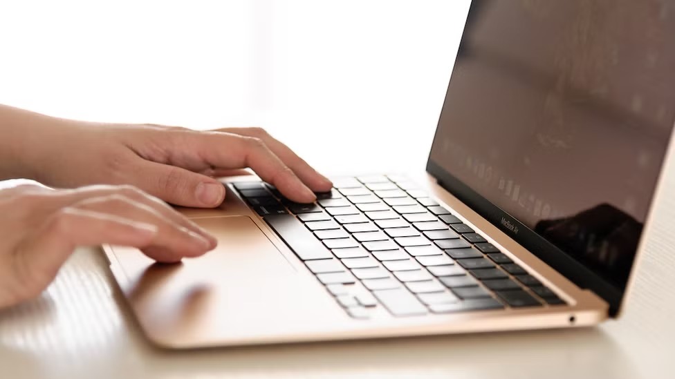 Hands typing on an Apple MacBook — users grant the Full Disk Access permission through a manual toggle in System Settings.