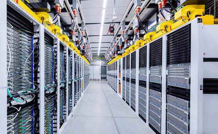 A bright high-density data center server aisle — the kind of AI server hardware at issue in both Apple's software crackdown and the federal smuggling case.