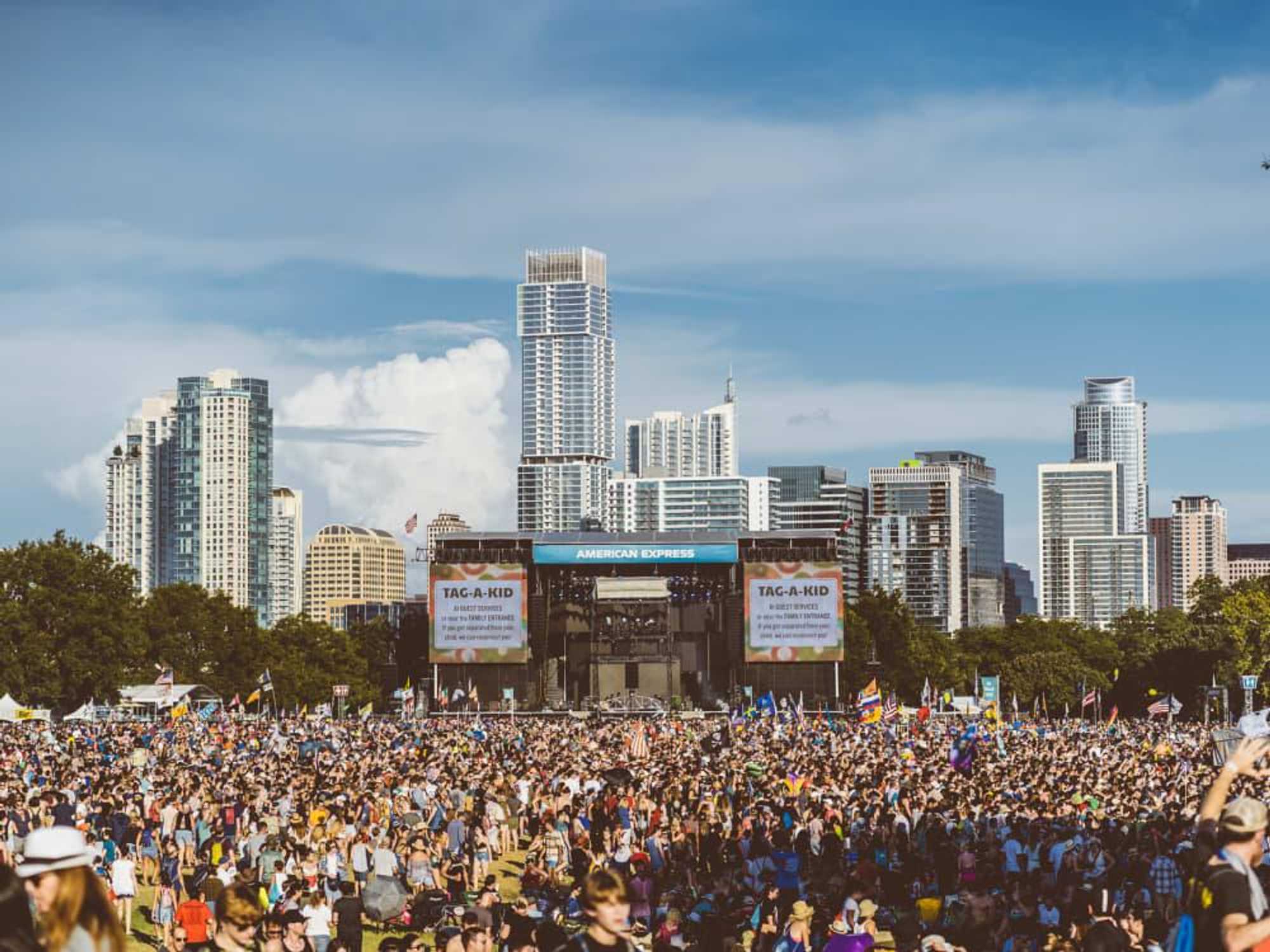 A daytime crowd before the American Express stage at Austin City Limits, the Austin skyline rising behind it