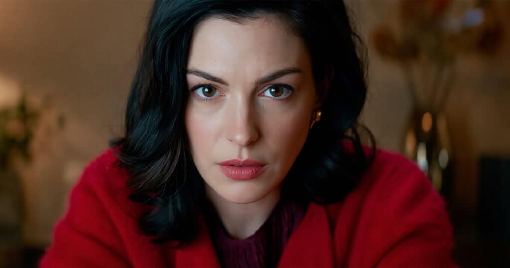 Anne Hathaway in a tense close-up, wearing a red coat, in a scene from the Amazon MGM thriller Verity