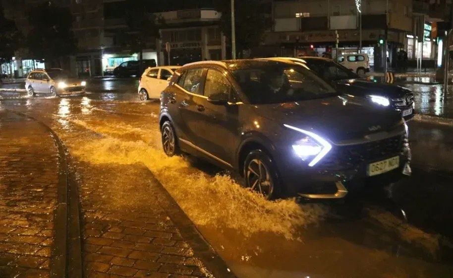Cars driving through deep floodwater on a street near Barcelona at night, headlights on