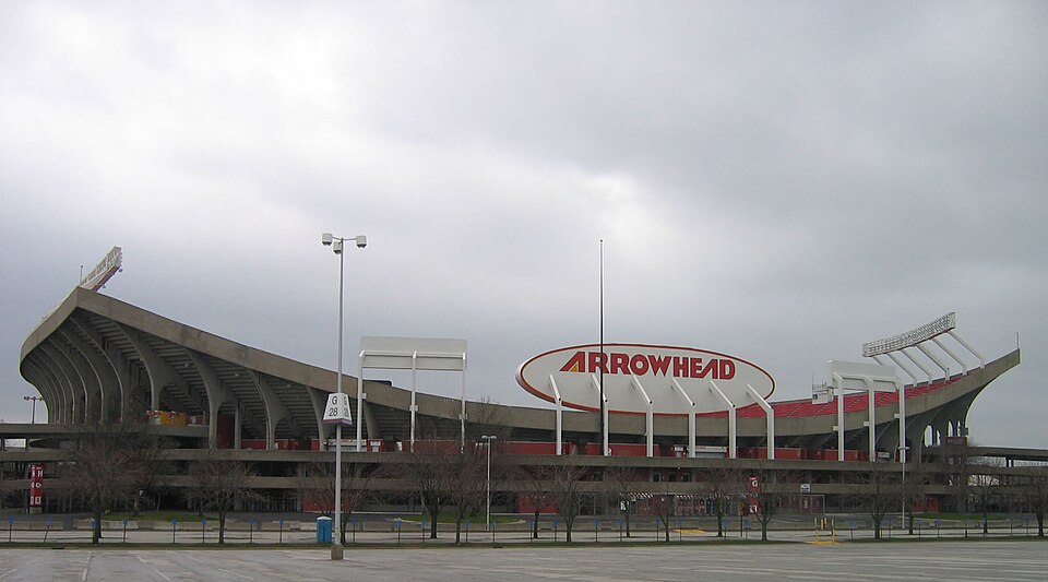 The Arrowhead Stadium sign in front of the stadium's concrete facade on an overcast day.