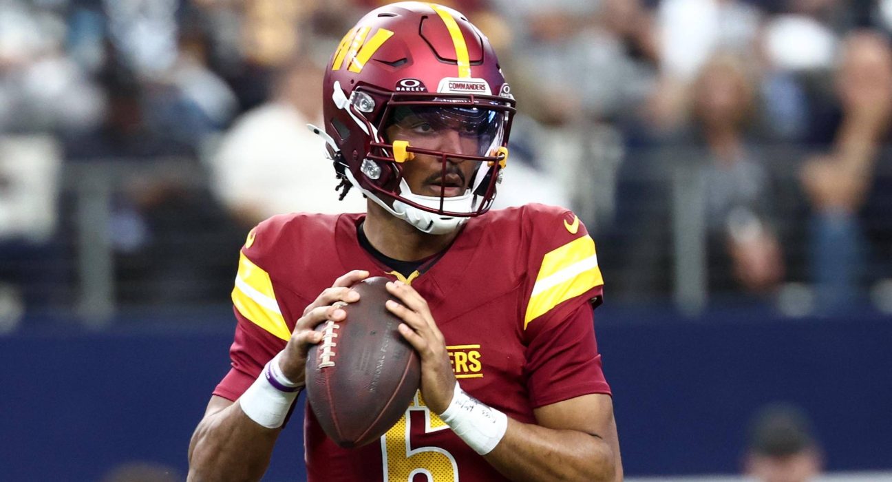Washington Commanders quarterback Jayden Daniels (5) in the burgundy home uniform, holding the football.