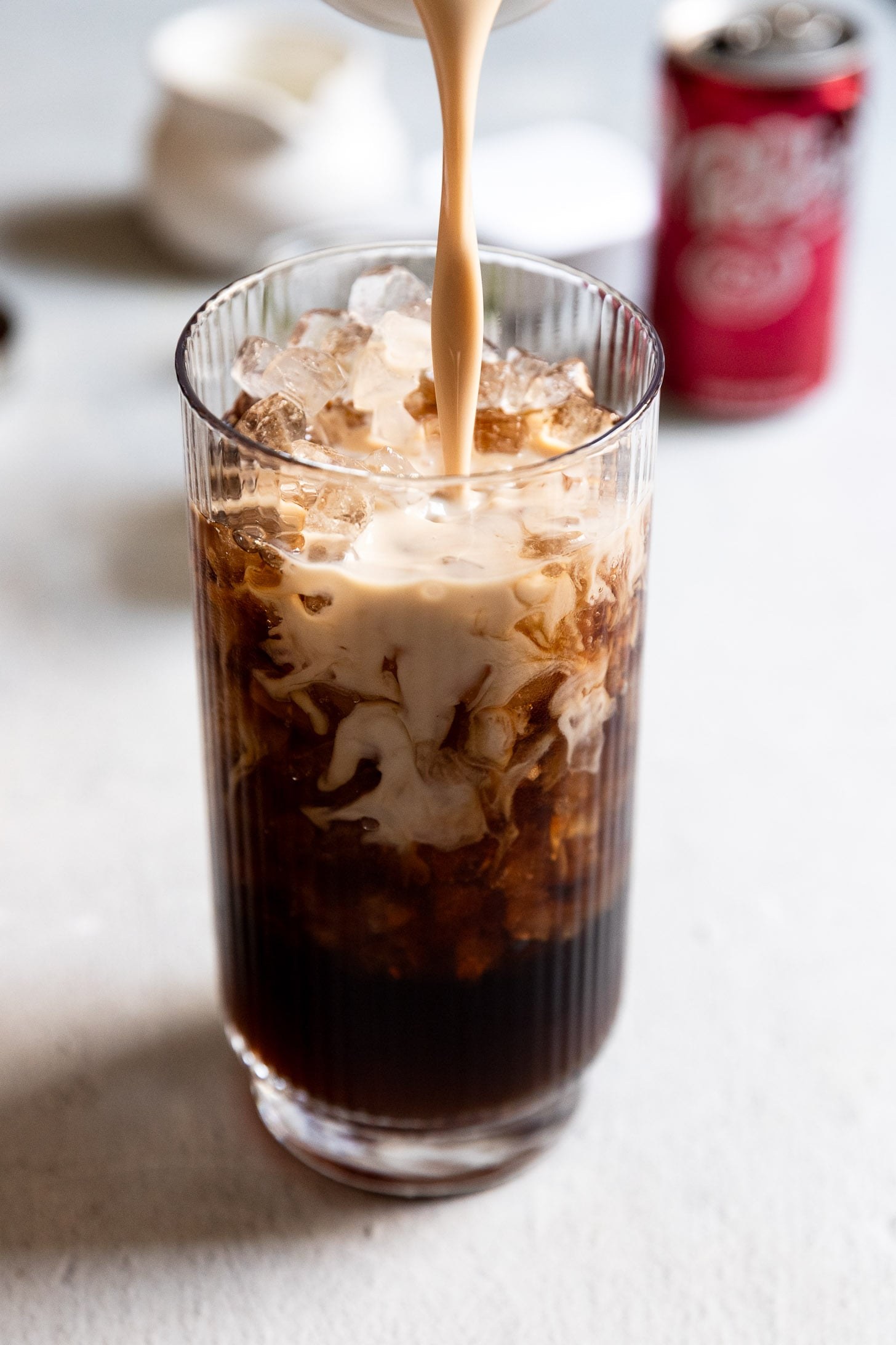 Cream being poured into an iced dirty soda, swirling through the glass