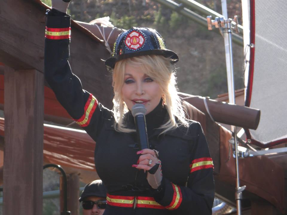 Dolly Parton smiling outdoors, wearing a patterned top and her signature blonde hair
