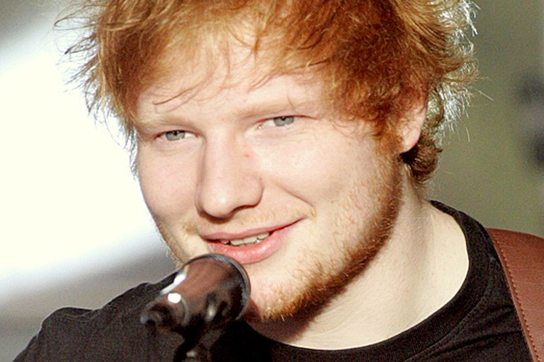 Ed Sheeran performing live on stage in front of a large crowd.