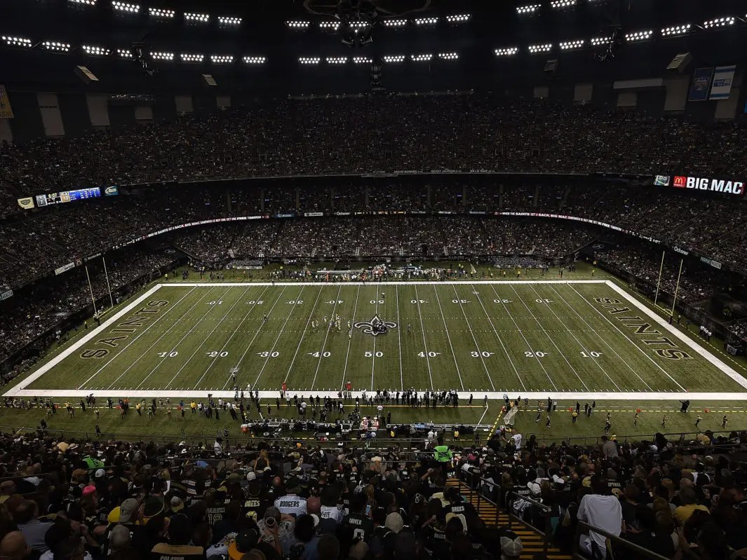The Caesars Superdome in New Orleans at night, packed with Saints fans under the lights.