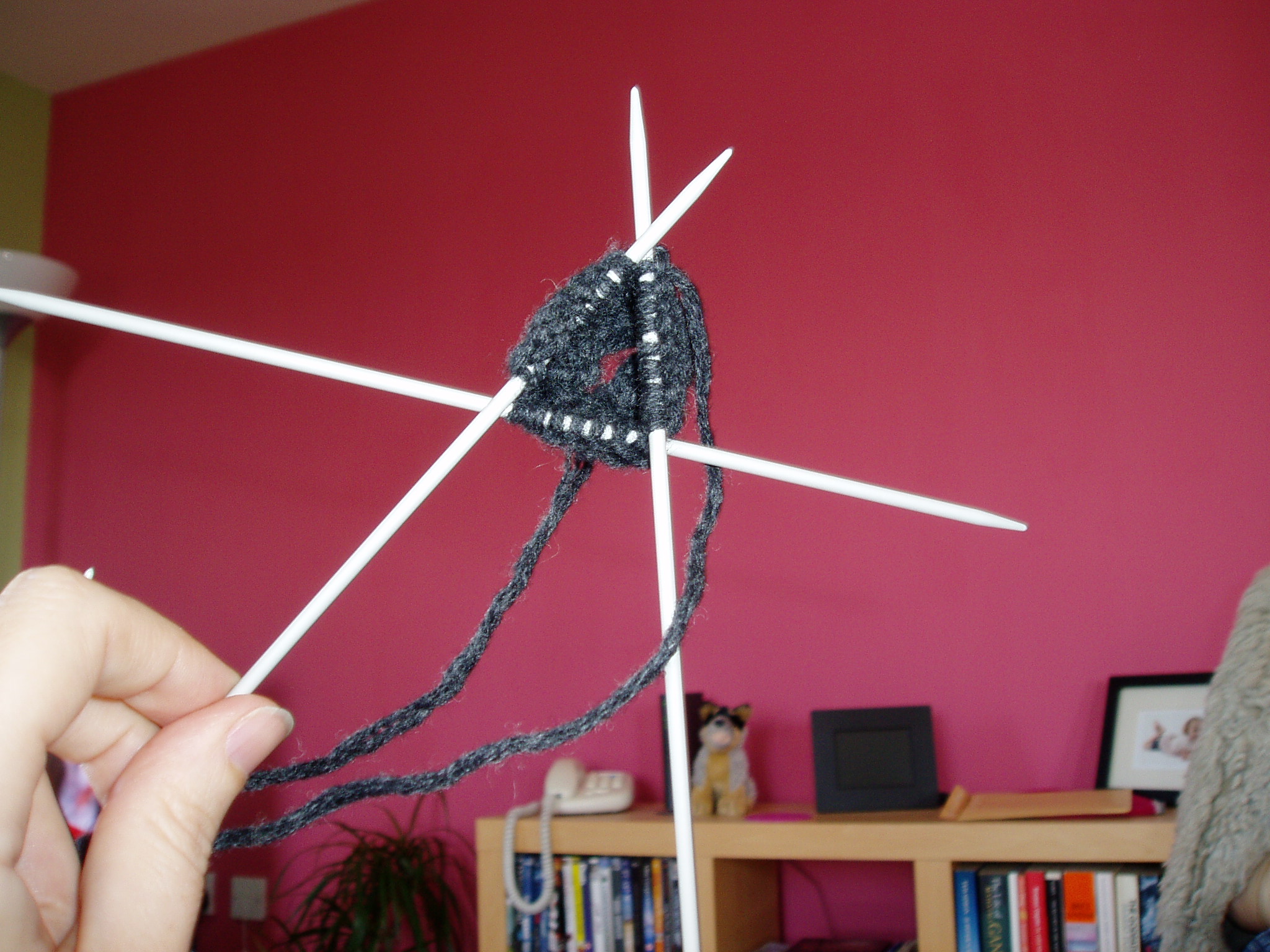 Close-up of a hand knitting dark yarn on double-pointed needles at home
