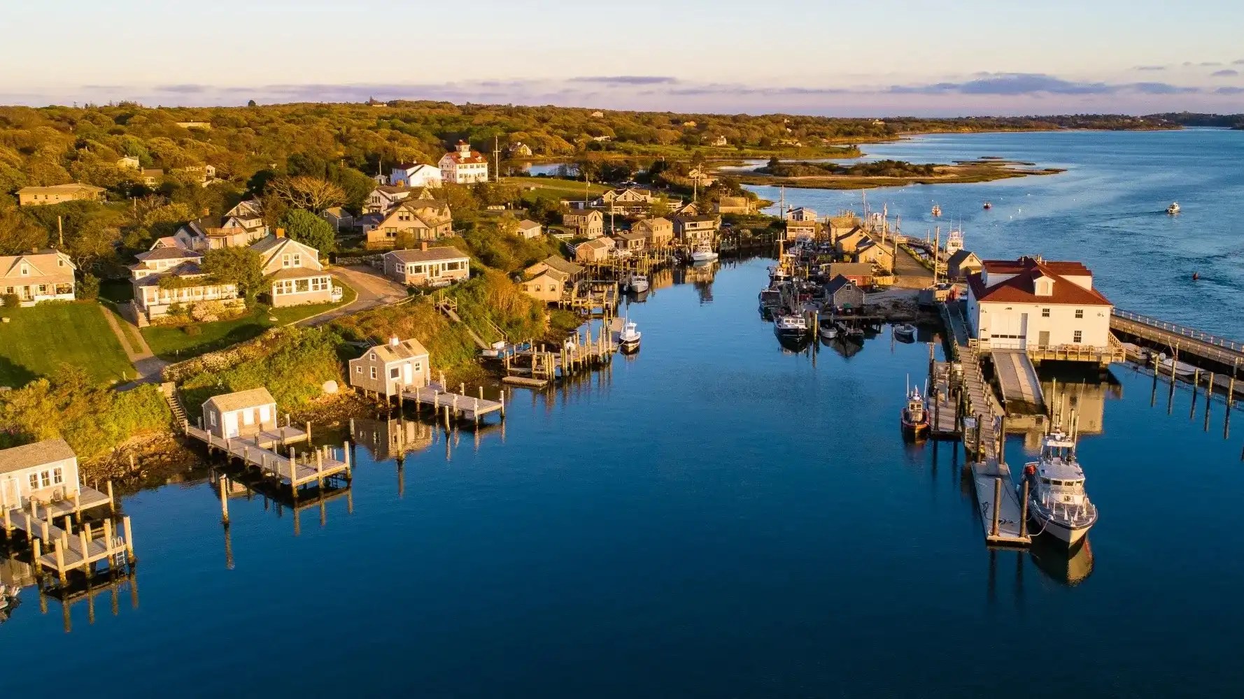 An aerial view of a Martha's Vineyard harbor town at golden hour, docks and boats on calm blue water