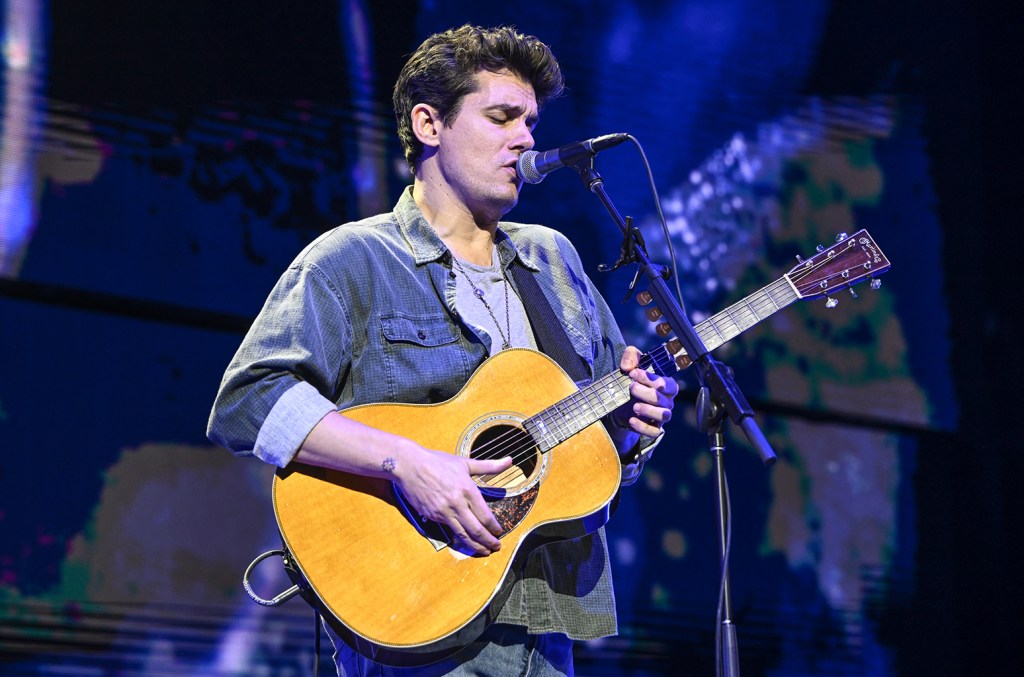 John Mayer playing acoustic guitar and singing into a microphone during a live show