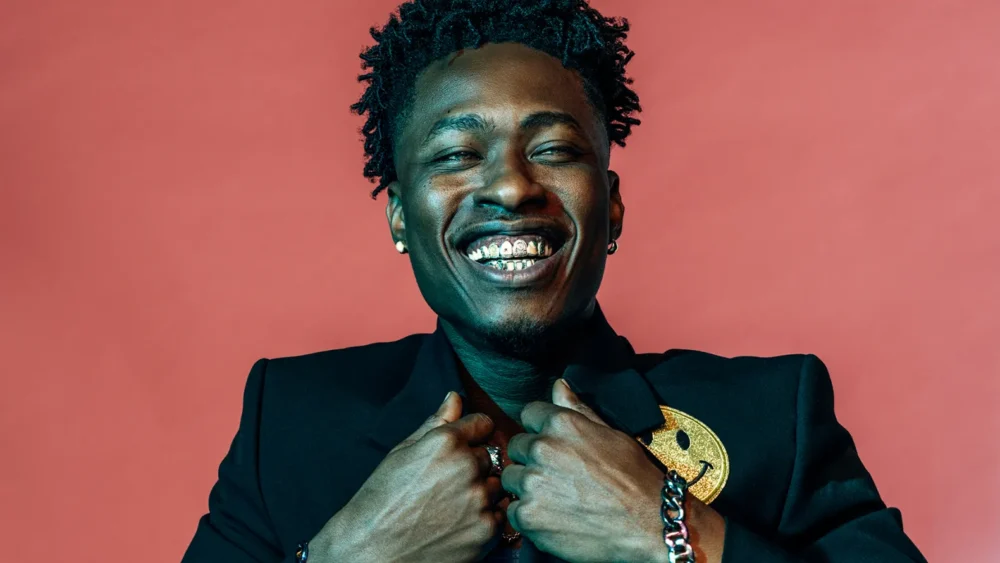 Lucky Daye smiling against a red backdrop