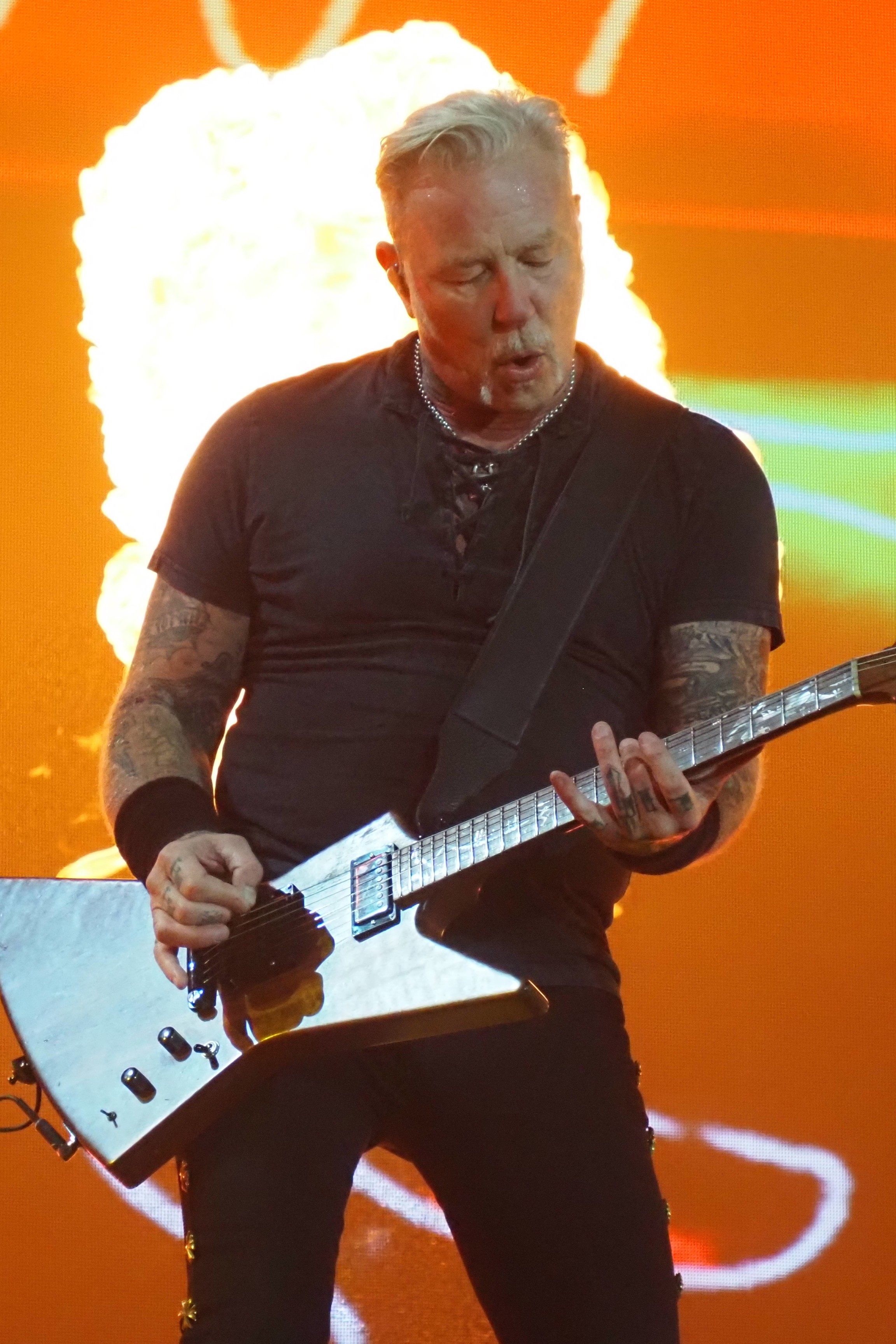 Metallica frontman James Hetfield performing on stage with pyro behind him