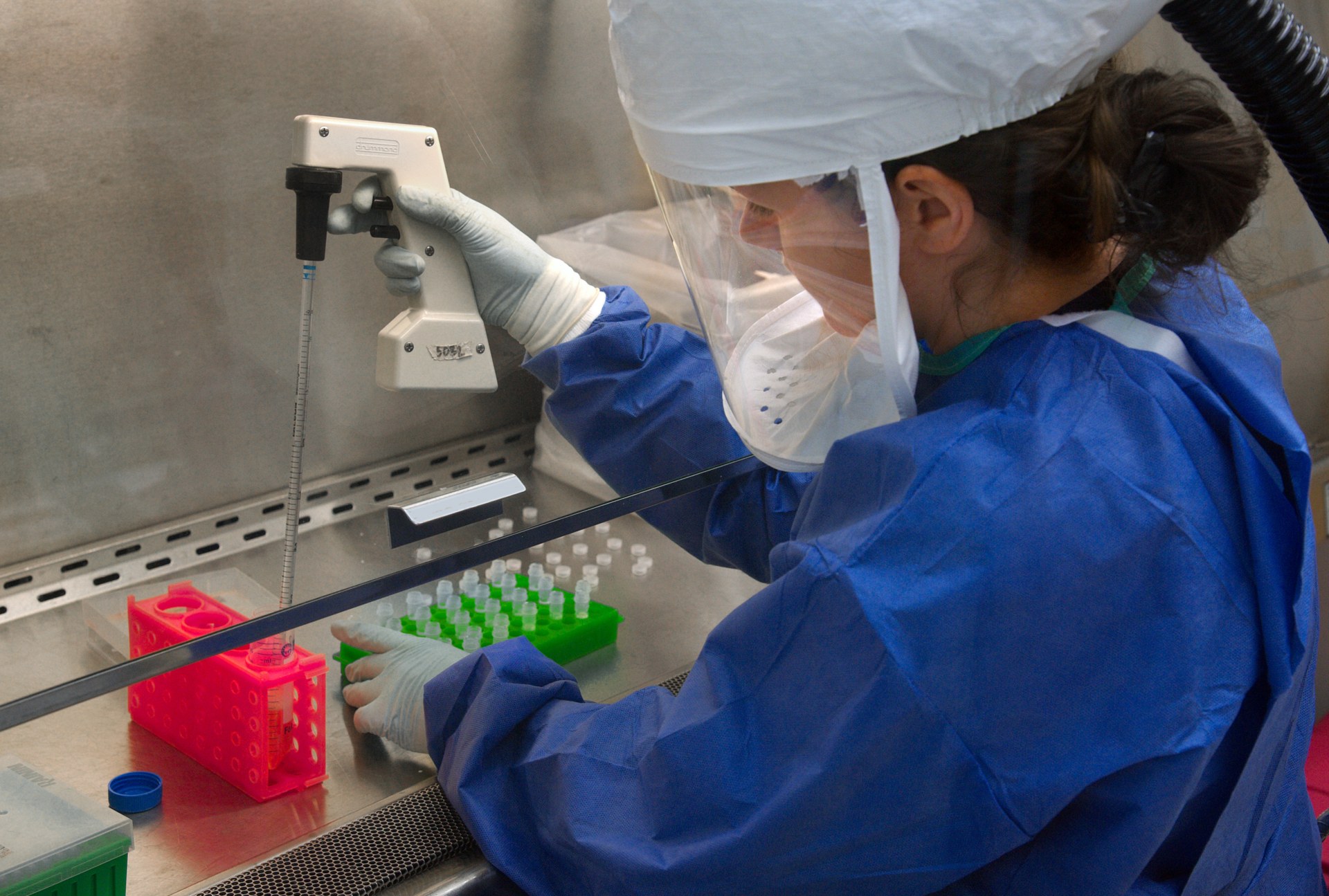 A CDC scientist in protective gear pipetting samples in a laboratory.