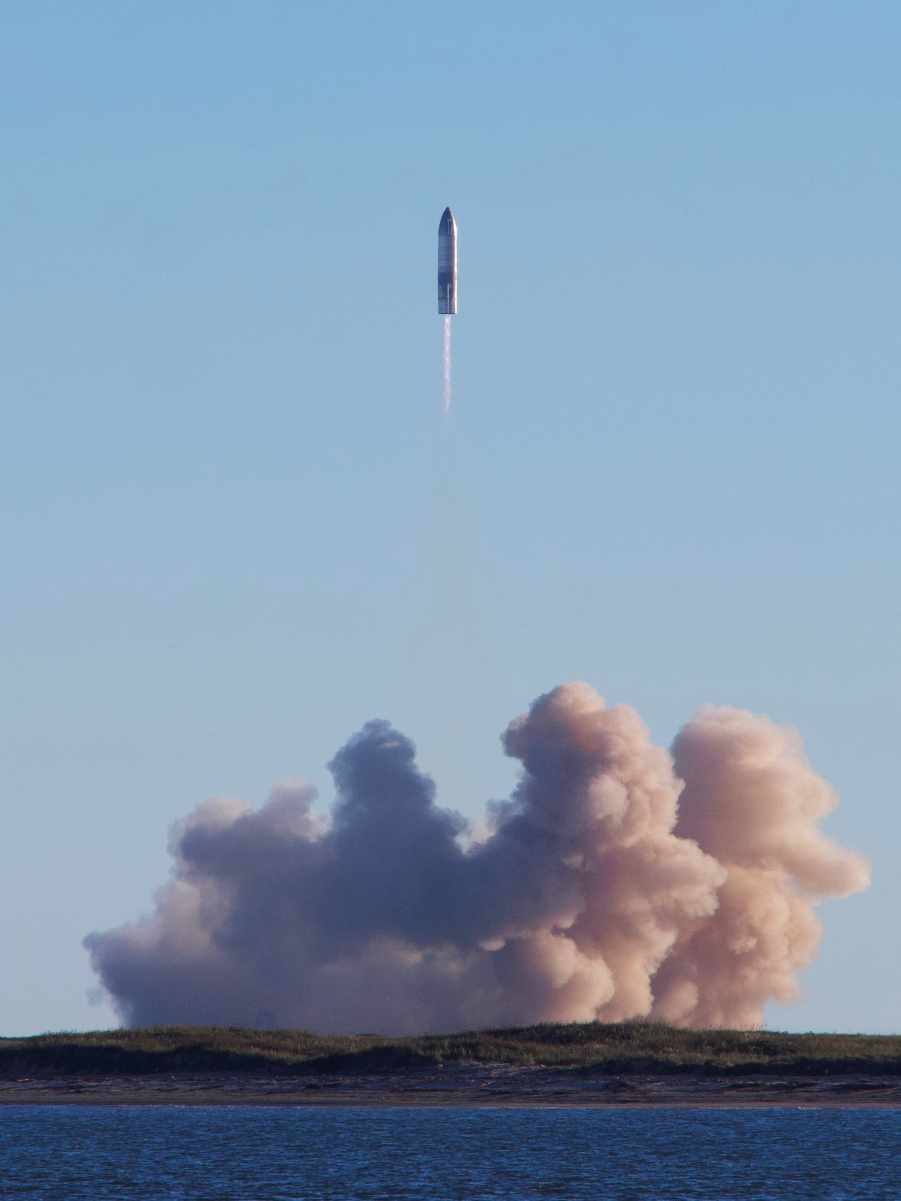 A SpaceX Starship rocket lifting off over the Texas coast, trailing a plume of smoke
