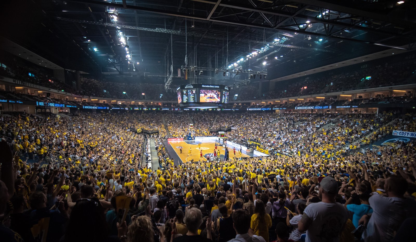 A capacity basketball arena crowd cheering under bright lights
