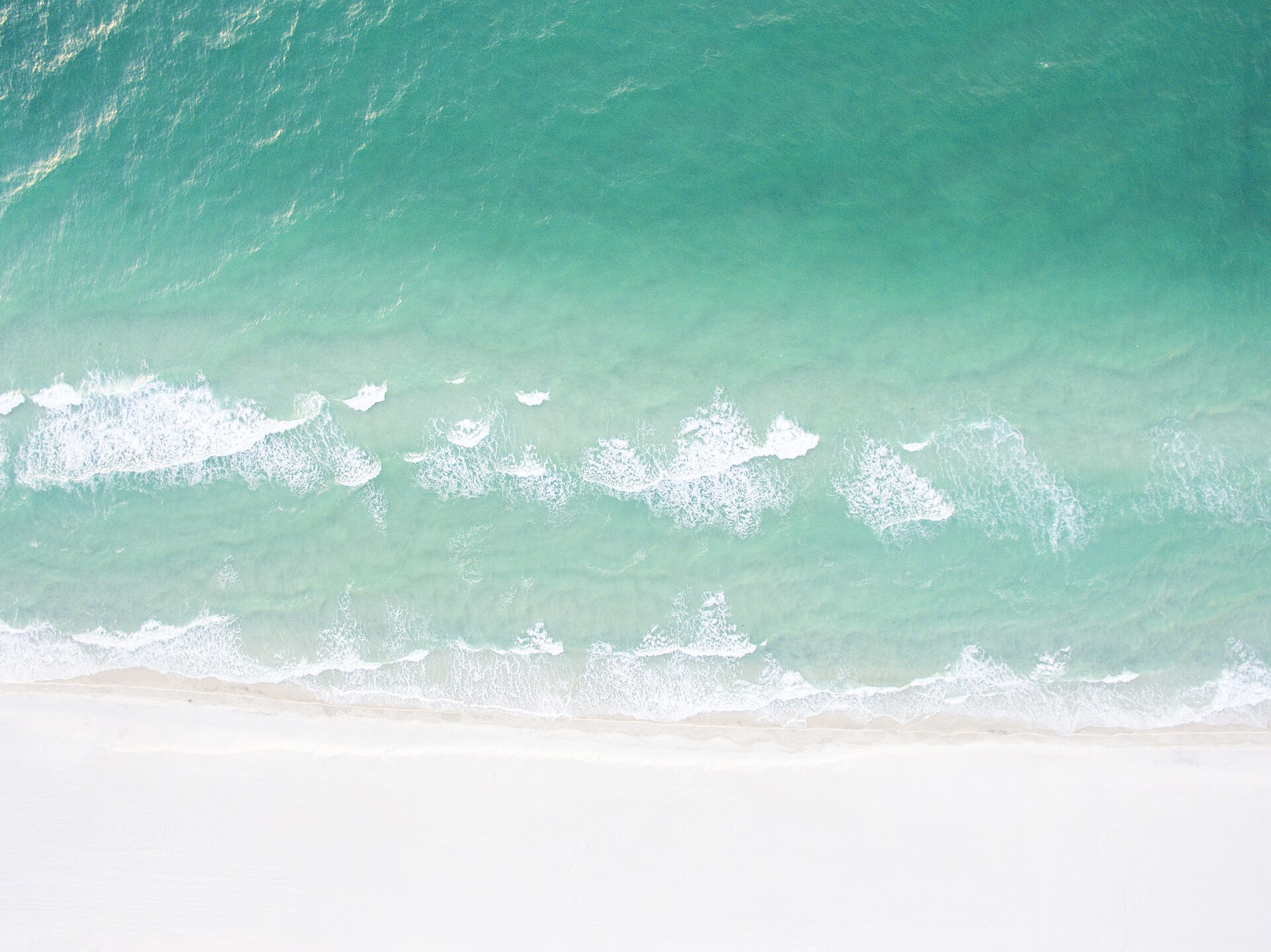 Aerial view of turquoise Gulf water meeting a white-sand beach at Gulf Breeze, Florida