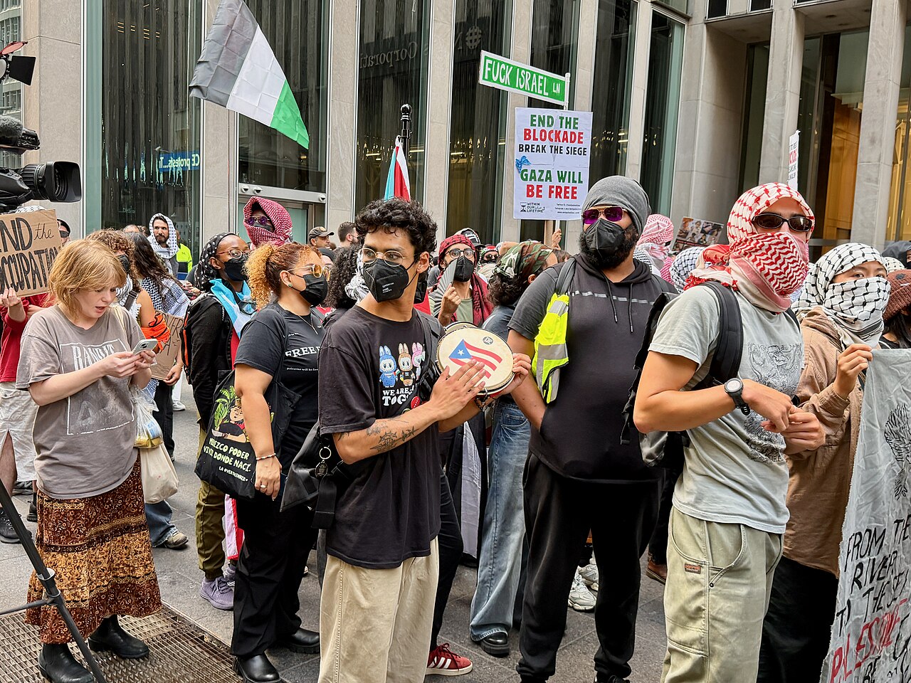 Masked pro-Palestinian demonstrators with signs and flags at a rally in New York City.