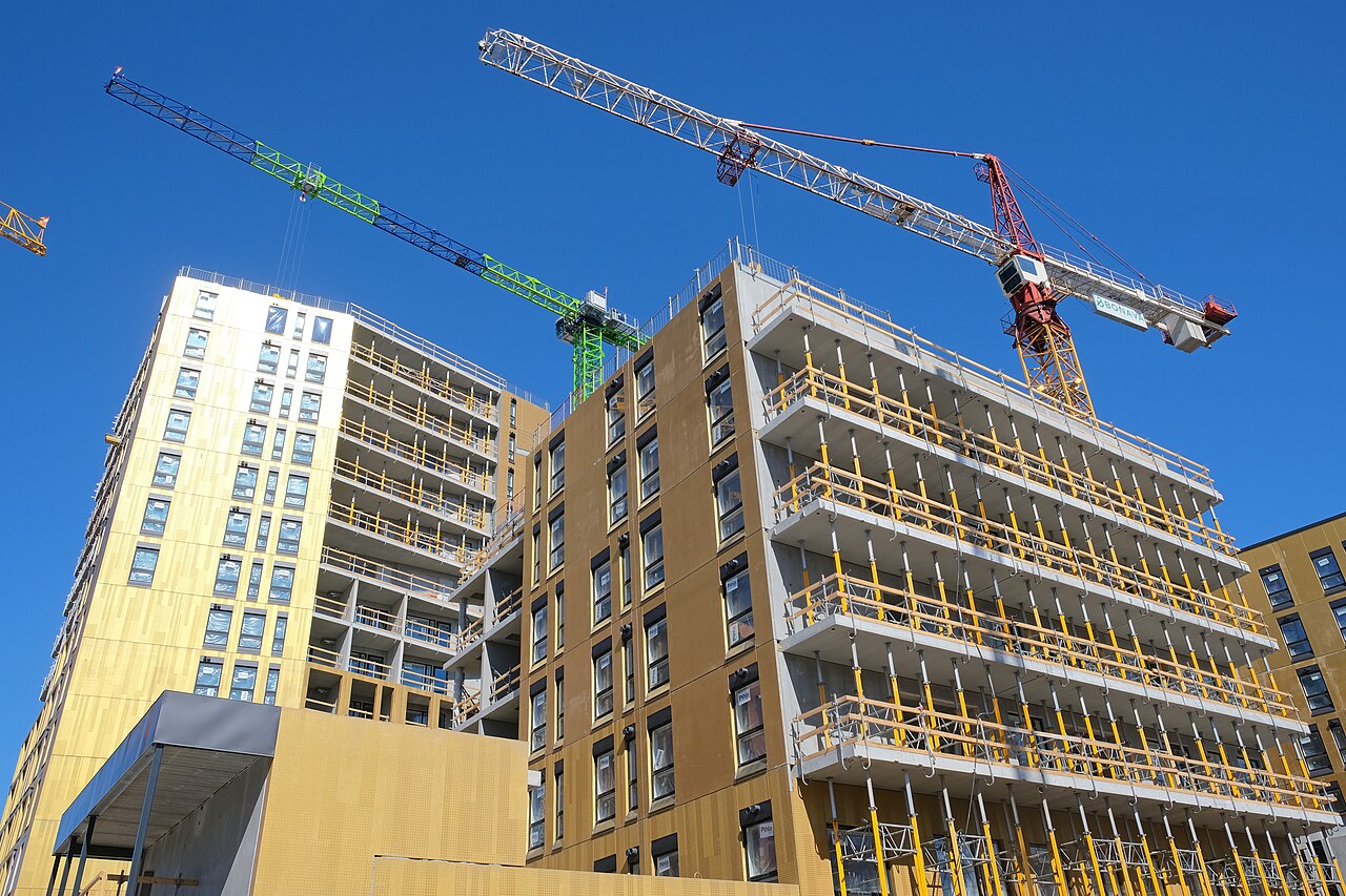 A residential construction site in bright daylight, with framing rising on new apartment buildings