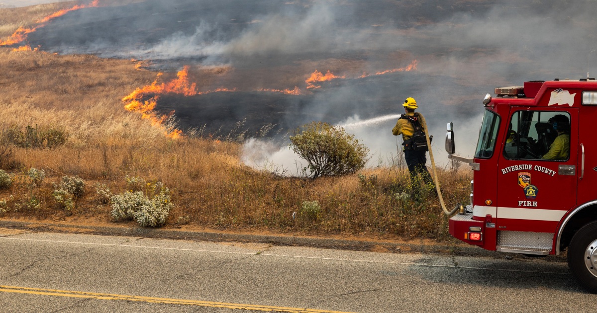 Wildfire burning across a Southern California hillside with smoke rising