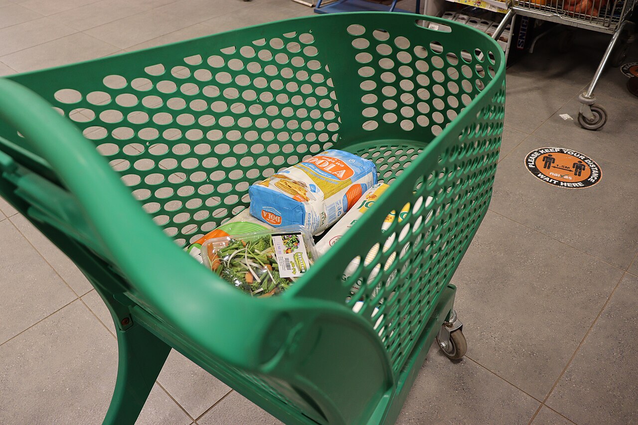 A shopping cart in a brightly lit supermarket aisle