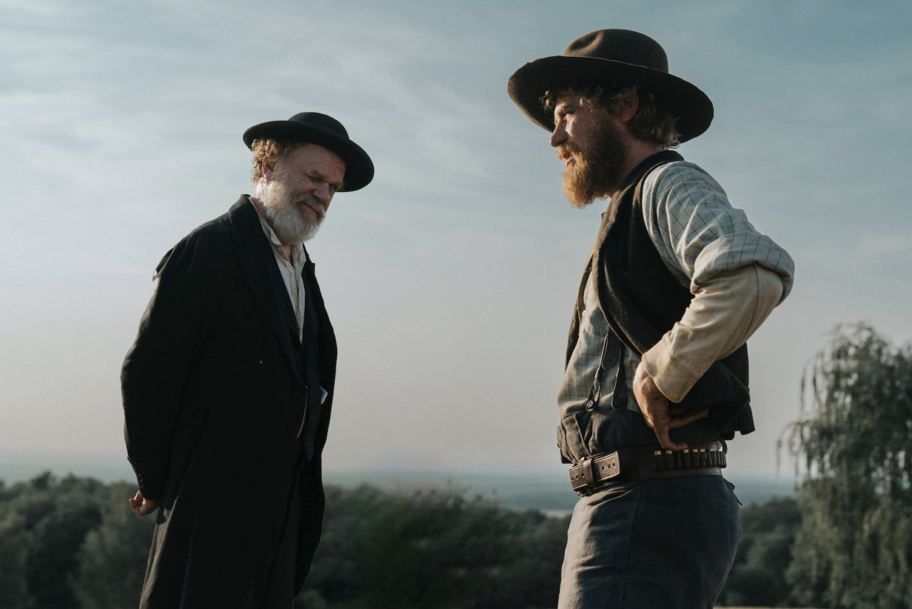 A still from A Prayer for the Dying — a dusty, smoke-hazed vision of 1870s Wisconsin under the twin threats of diphtheria and wildfire