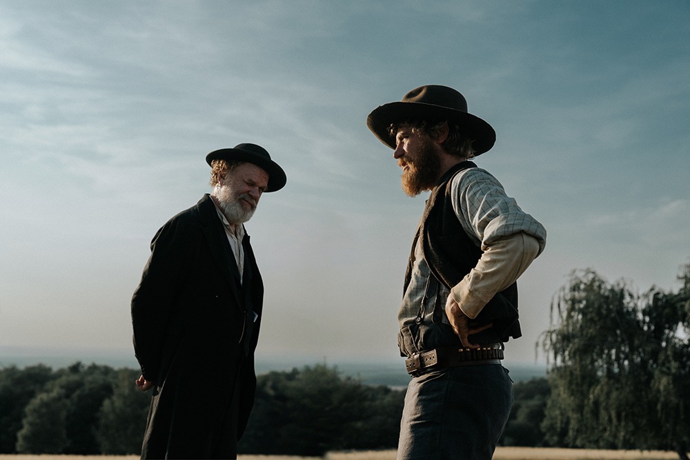 Johnny Flynn as Jacob Hansen in A Prayer for the Dying, weathered and watchful in 1870s Wisconsin