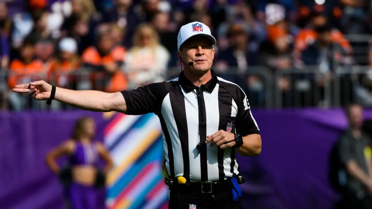 An NFL official in stripes signals on the field during a daylight game