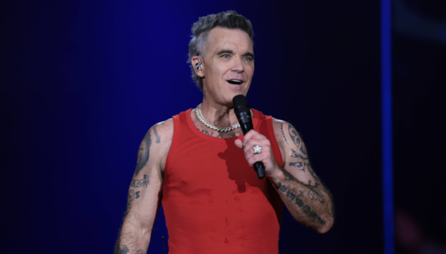 Close-up of Robbie Williams performing with a microphone in 2026.