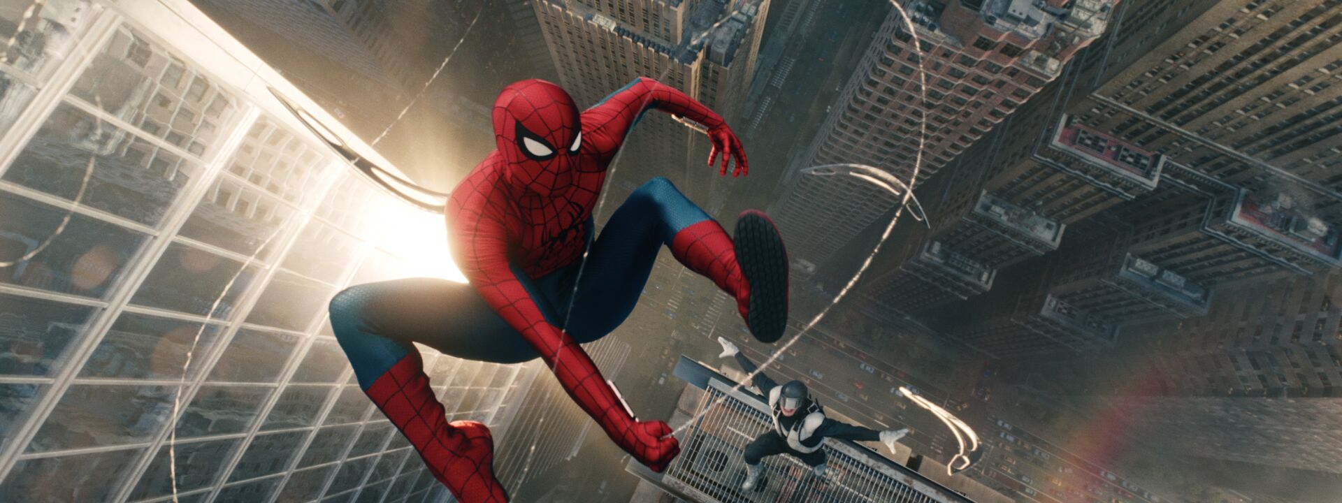 Spider-Man swings above the sunlit New York City skyline in a still from Spider-Man: Brand New Day, with another figure visible on a rooftop below