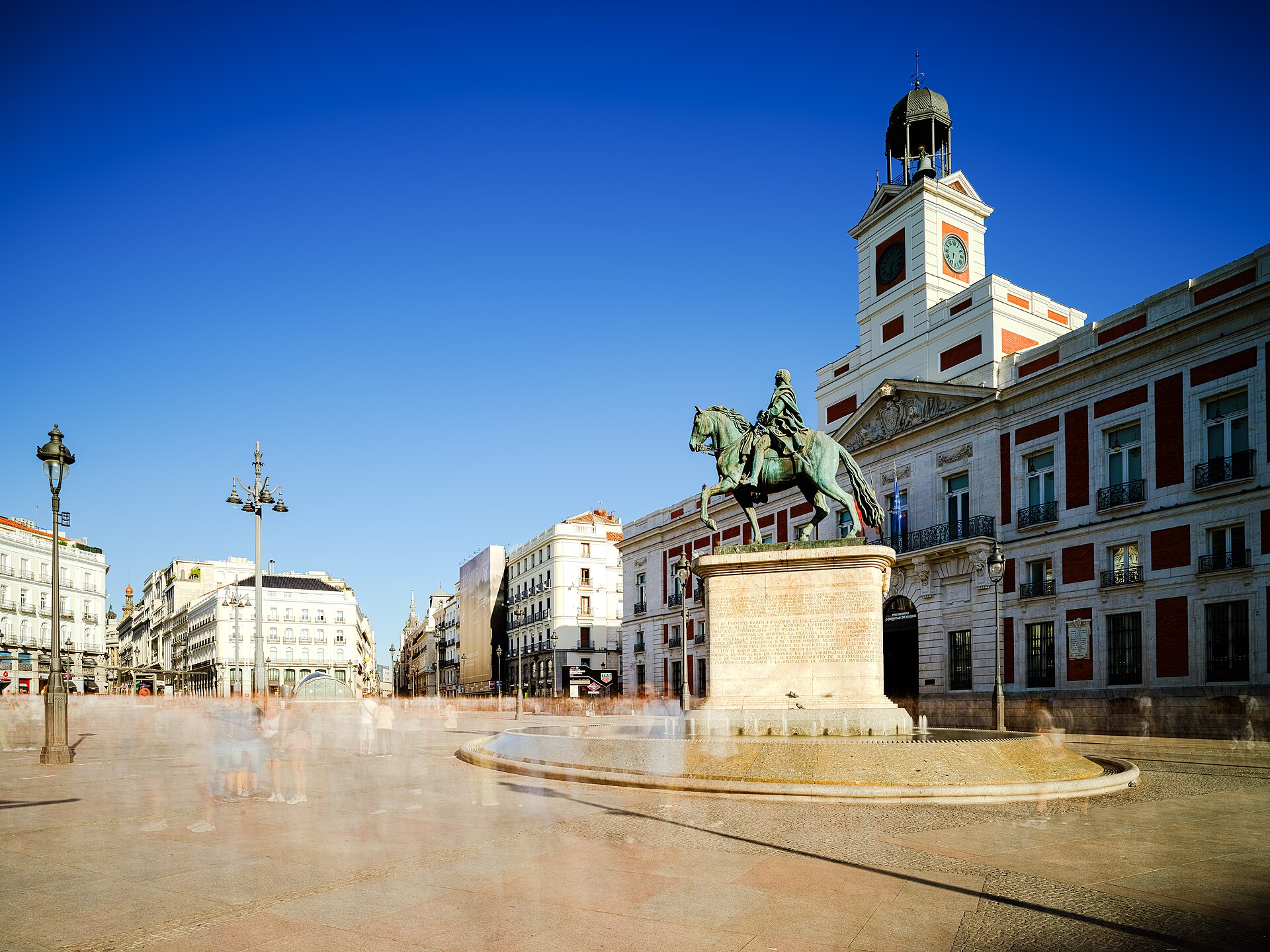 Puerta del Sol in Madrid on a bright day, with the equestrian statue of Charles III and the clock tower of the Real Casa de Correos — the square where housing protesters camped in the days before the snap election call.