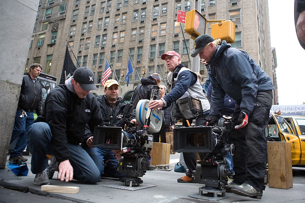 A television film crew with cinema cameras shooting on a New York City street, a yellow cab passing behind